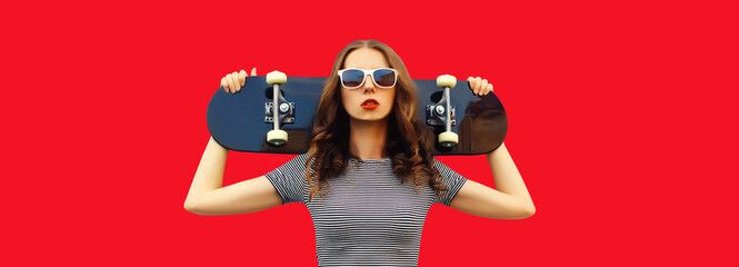 Portrait of stylish young woman posing with skateboard on red background