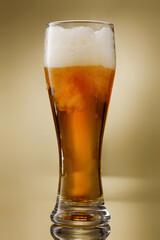 Beer. Glass of fresh and cold beer with drops. Pouring craft golden beer on a golden background. ...