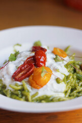 Close-up of Italian trofia pasta with pesto, burrata cheese and cherry tomatoes served on a white plate. Italian/Ligurian cuisine, selective focus, copy space