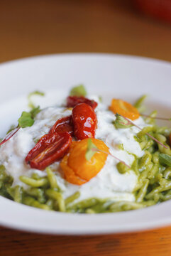 Close-up of Italian trofia pasta with pesto, burrata cheese and cherry tomatoes served on a white plate. Italian/Ligurian cuisine, selective focus, copy space