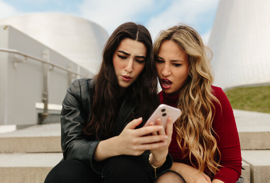 Two women reacting to smartphone content outdoors