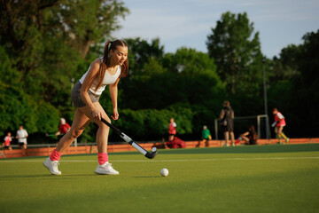 Obraz premium girl hockey player plays field hockey on a sunny day, the hockey player hits the ball with a stick