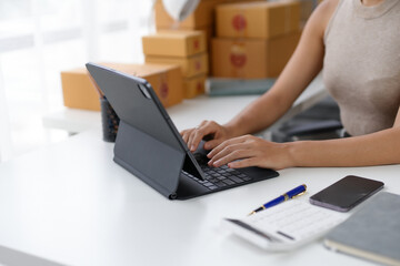 Woman working on a tablet at a desk with shipping boxes in the background, illustrating e-commerce and small business operations.