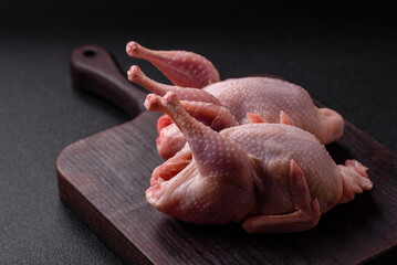 Whole raw quails with salt, spices and herbs on a dark concrete background