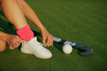 girl hockey player tying sneakers on the field hockey field, concept of playing field hockey