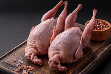 Whole raw quails with salt, spices and herbs on a dark concrete background