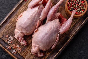 Whole raw quails with salt, spices and herbs on a dark concrete background