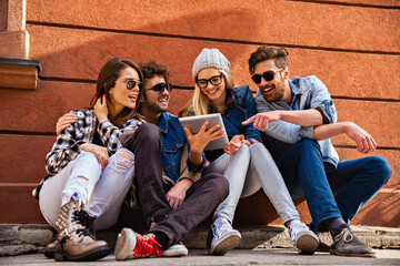 Group of friends sitting outdoors laughing and looking at a tablet