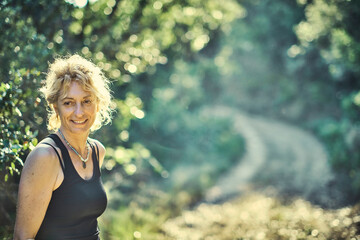 A woman with blonde hair is smiling in a forest.