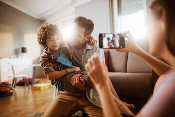 Happy family moment with mother taking photo of father playing with son in living room