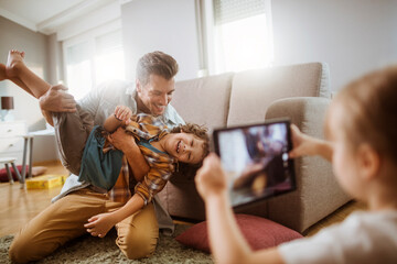 Father playing with son while being photographed by daughter at home
