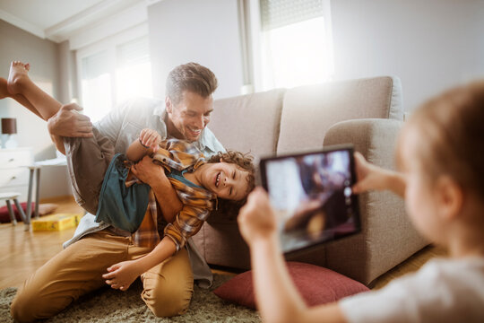 Father playing with son while being photographed by daughter at home