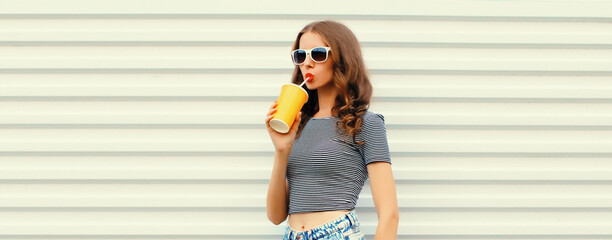 Stylish young woman drinking fresh juice wearing glasses looking away on white background