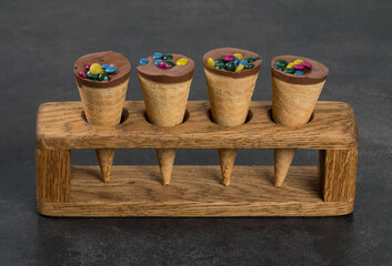 Vegan Waffle cone, with chocolate nut cream and colored dragees. On a wooden serving stand. Close up