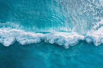 An aerial perspective captures a powerful ocean wave breaking against the horizon, with a clear blue sky above
