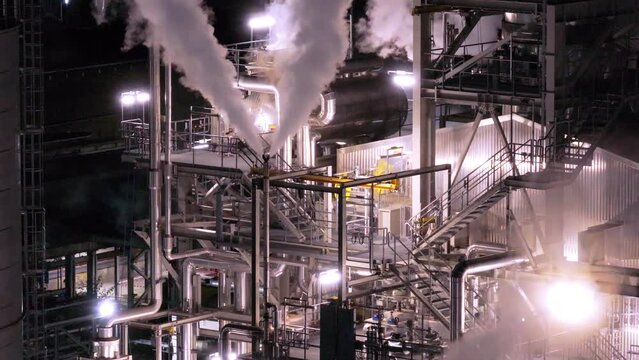 Medium aerial shot of paper mill industrial plant with plumes of steam coming from chimneys at night