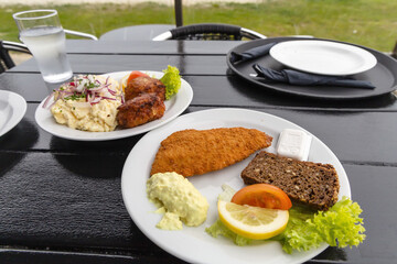 Seafood restaurant on the seashore. White plate with fish patties, fish fillets and potato salad.