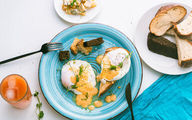 Summer healthy and delicious breakfast: eggs Benedict on toast with pea greens on a blue plate with orange or grapefruit juice and cutlery. selected focus. Close-up, top view.