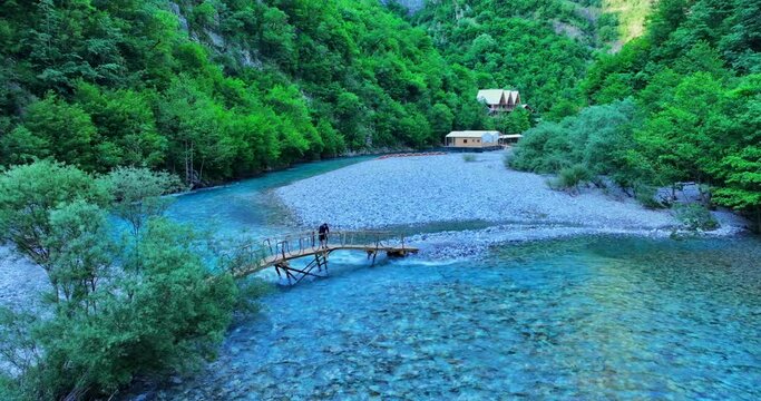 Shala river in northern Albania with clear blue waters and a young man taking photographs over a wooden bridge 