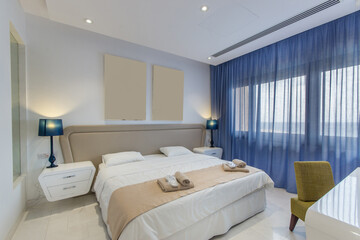 Fototapeta premium Cozy bright bedroom of the hotel with a wide bed and a large window.