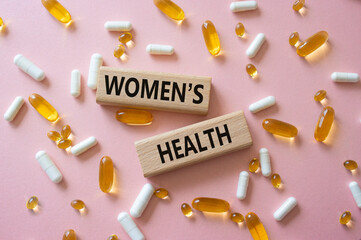 Womens health symbol. Concept word Womens health on wooden blocks. Beautiful pink background with pills. Medicine and Womens health concept. Copy space