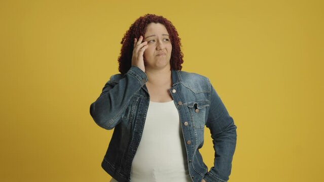 Pensive young woman 20s years old in denin jacket and white t-shirt posing looks around thinks scratches at temple comes up with ideas raised finger up isolated on yellow background in studio. People 
