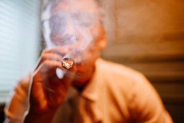 Valmiera, Latvia - September 9, 2023 - Close-up of a man smoking a lit cigar, with smoke swirling...