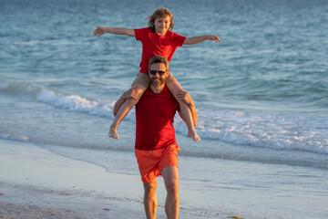 Son sits on fathers shoulders piggyback ride. Outdoor portrait of happy father and son walking on...