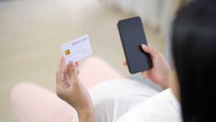A portrait of happy Asian pregnant woman using a mobile phone device with credit card, shopping online in bedroom at home. Having a baby. Family people lifestyle. Mom love.