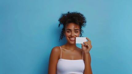 Front shot of a lovely smiling woman holding a white credit card, standing against blue background