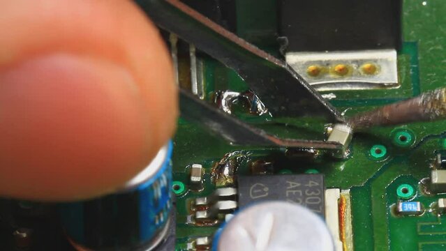 Technician repairs electronic circuit board with soldering iron. Desoldering a surface mounted resistor using a soldering iron
