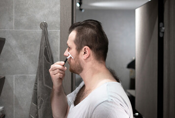 Shaves with a blade, a man shaves his beard with a razor in the bathroom in the apartment
