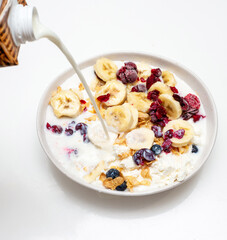 Bananas with blueberries, cottage cheese and raisins in a plate in the kitchen. Pour milk into muesli with cottage cheese and cherry and black berry fruits