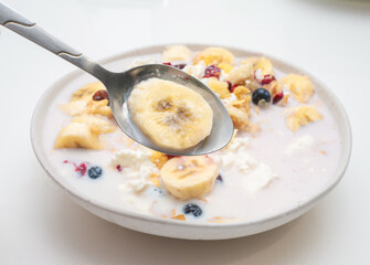 Top view, Bananas with blueberries, cottage cheese and raisins in a plate in the kitchen. With milk muesli with cottage cheese and cherry and black berry fruits