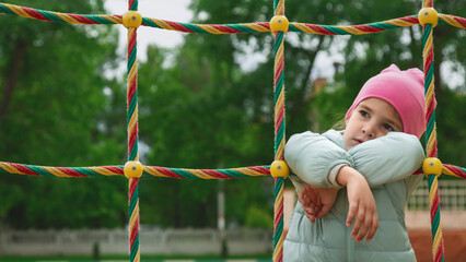 Little child girl in casual clothes climbing network of ropes on sports ground