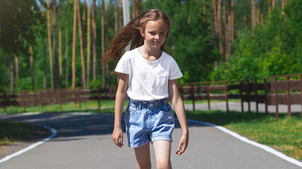 Positive pretty little girl going road on park in the white t-shirt and jeans shorts sunny weather warm season.