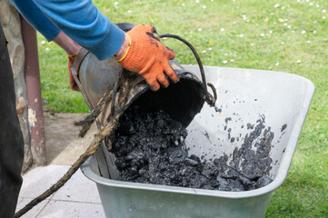 A man pours mud from a bucket into a wheelbarrow from the bottom of a well.