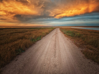 ground road on the wild spit in lagoon under burning and dramatic clouds