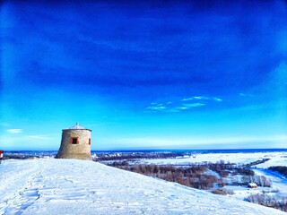 Winter Vista From an Ancient Stone Tower Overlooking a Snowy Landscape. An old stone tower provides a view of a frozen river and wintery fields at dusk