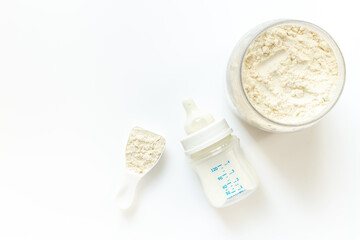 Jar of powdered milk for baby food with bottle of milk and spoon, top view