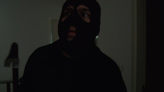 The creepy thief with black mask holding crowbar and looking around inside the room for robbery, home security to prevent the crimination, criminal impact on economic society.
