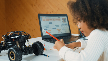 African girl writing car model structure while laptop display code. Smart student working by using...