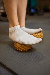 Person stands on yoga mat with feet on massage ball