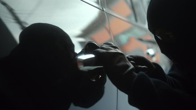 The creepy thief with wearing black mask using tool to break unlock the door's handle of vehicle, robber stealing a car, car security to prevent the crimination, criminal impact on economic society.
