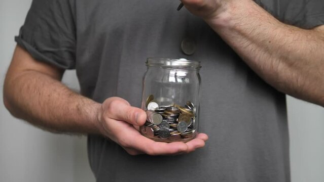 A man throws a coin into a piggy bank from a glass money jar in slow motion. Concept of saving and storing money. Financial crisis, saving cash