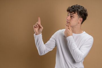 Portrait of one caucasian man 20 years old looking to the camera in front of almond color studio background smiling wearing casual shirt point on copy space