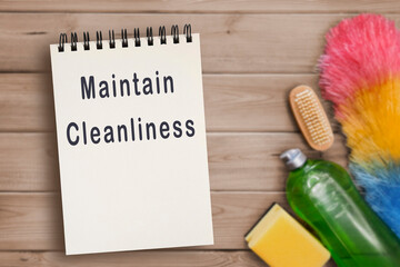 SMaintain cleanliness concept. Text in spiral black notepad on blurred table background with bottle of detergent, kitchen sponge, dust brush, dish brush. Planning and scheduling household chores.