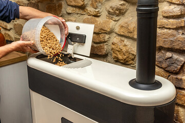 Man filling a biomass boiler or stove with wood pellets. Biofuel heating system at home.