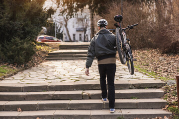 Man Carrying His Bicycle Up Stone Steps in Urban Park