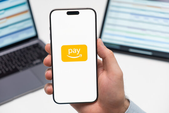 PRAGUE, CZECH REPUBLIC - JANUARY 21 2024: Amazon pay logo on the screen of smartphone in mans hand on the workplace background. 
